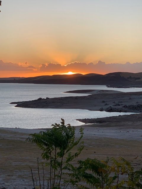 Sunset over a serene lake with a calm shoreline, capturing peaceful outdoor scenery and tranquil water views for outdoor recreation and leisure themes.