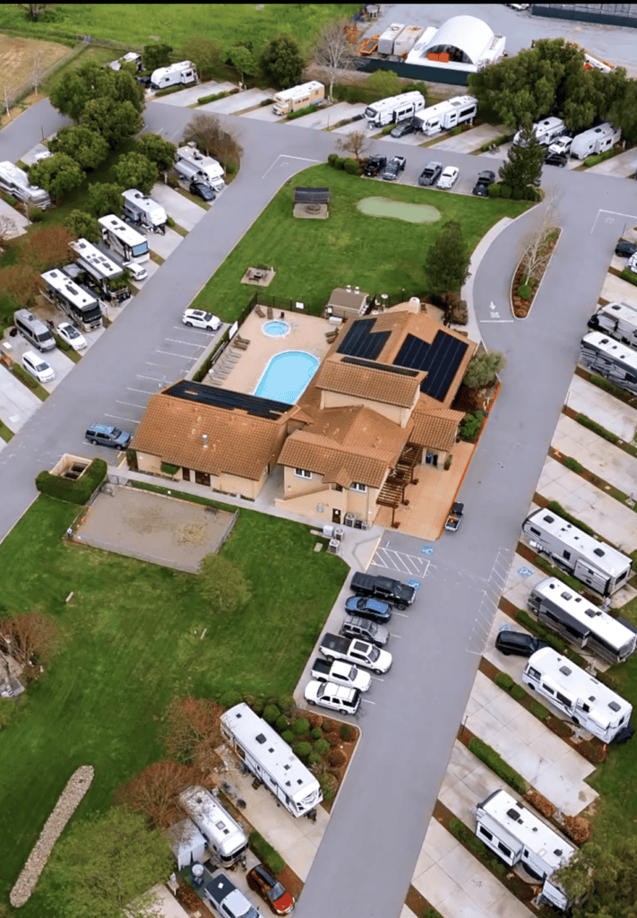 Aerial view of FreeWheelers RV community featuring RV parking, amenities, pool, and clubhouse with lush green lawns and organized pathways, showcasing a vibrant, family-friendly recreational vehicle park.