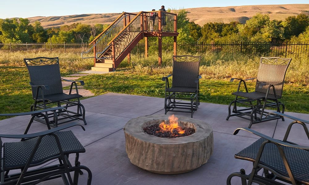 Cozy outdoor fire pit area with metal chairs, overlooking scenic rolling hills and greenery, ideal for relaxation and social gatherings in a peaceful outdoor setting.