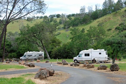 Two RVs parked along a scenic road at Del Valle Regional Park in Livermore, CA, surrounded by lush green hills and trees, ideal for outdoor adventures and camping.