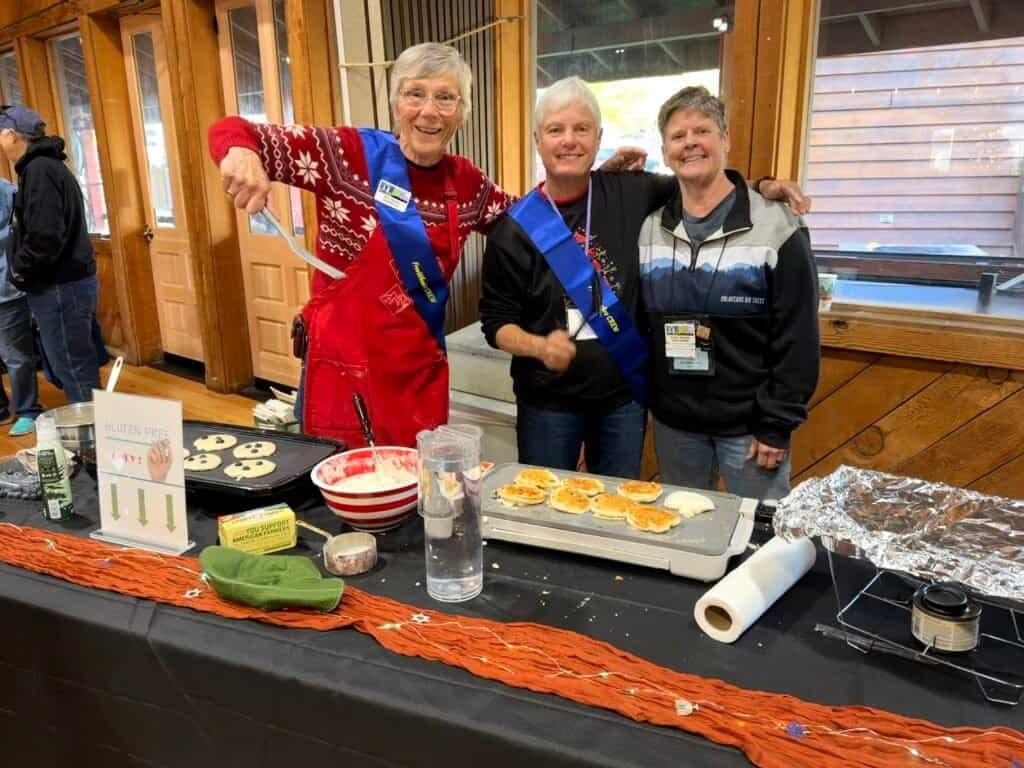 Enjoying RVing, traveling, camping, nature with women at a gathering, smiling and wearing blue sashes.